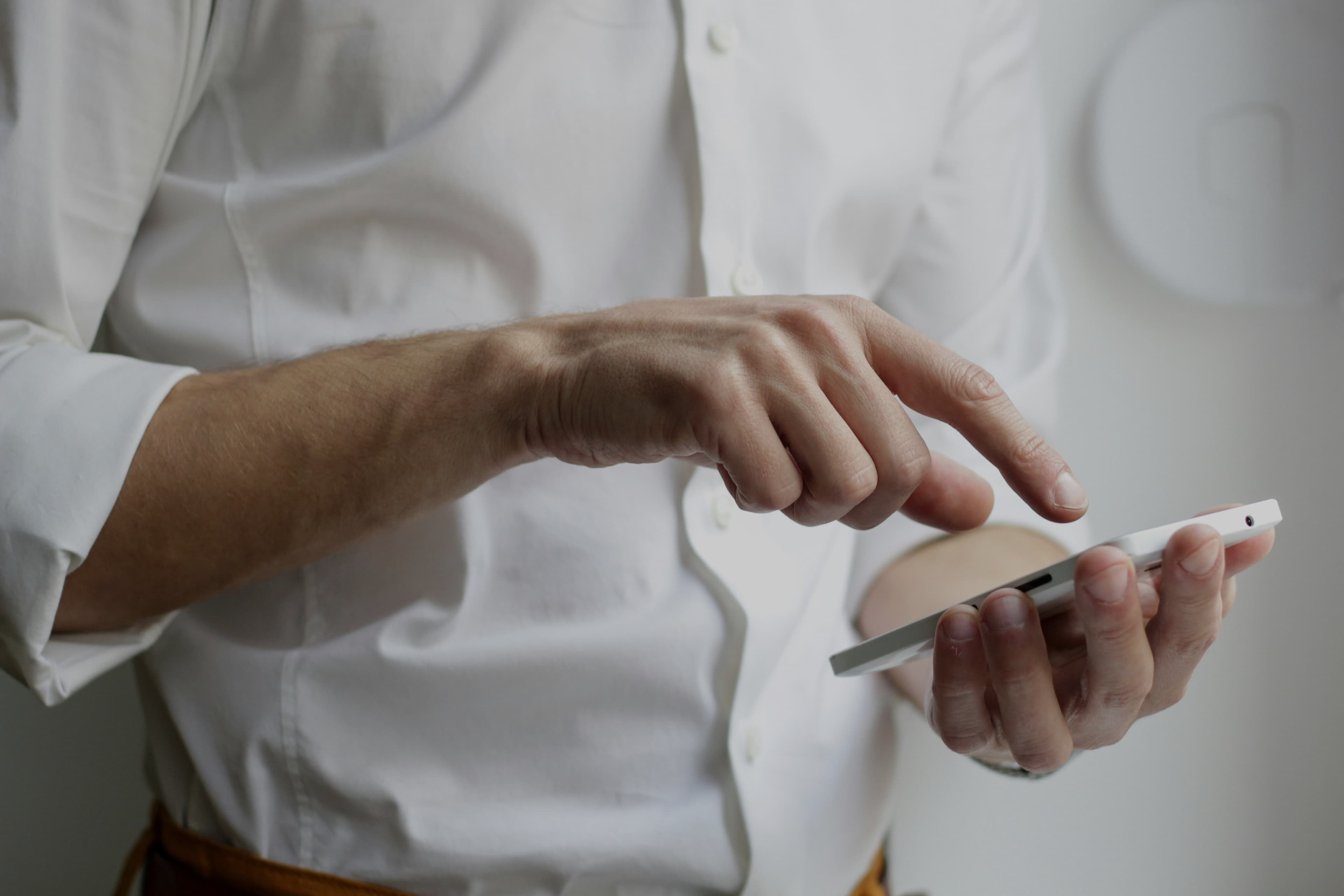 A person in a white shirt is using a mobile phone, holding it in one hand and tapping the screen with the other.