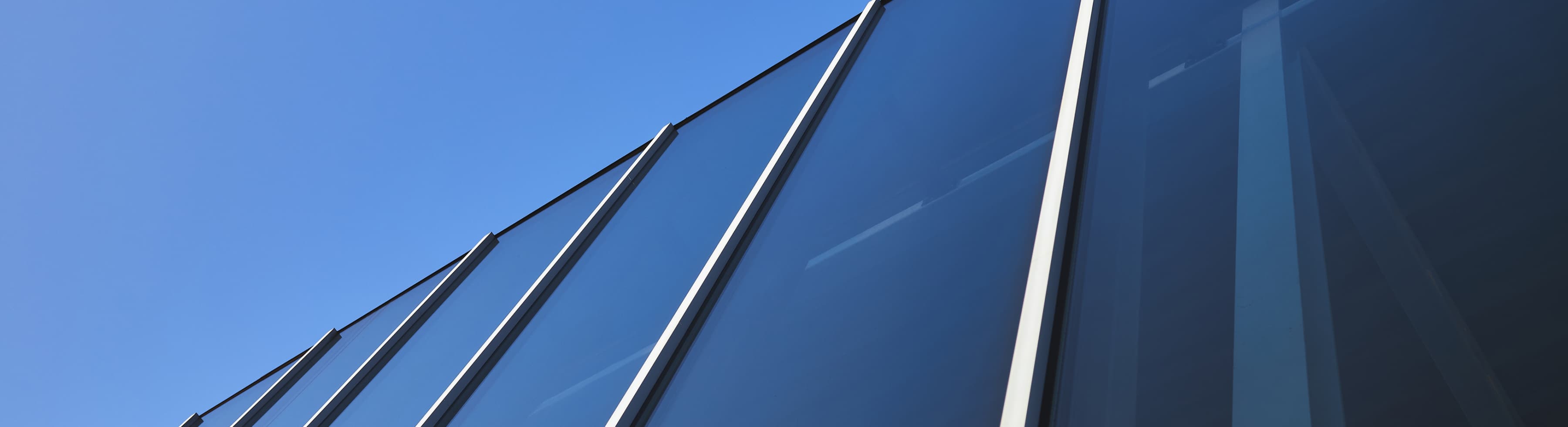 Close-up of a modern glass building façade with vertical metal beams against a clear blue sky.